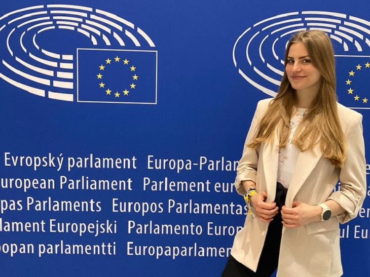 Fiatal lány az Európai Parlament kék alapon csillagos vászna előtt áll